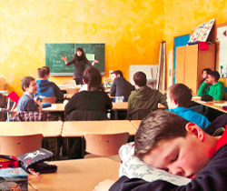  Imagen de una profesora con sus alumnos en un aula y uno de ellos dormido sobre el pupitre 