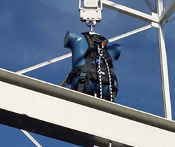 Imagen de un maniquí para ensayar caídas de altura con un arnés y colgando de una estructura