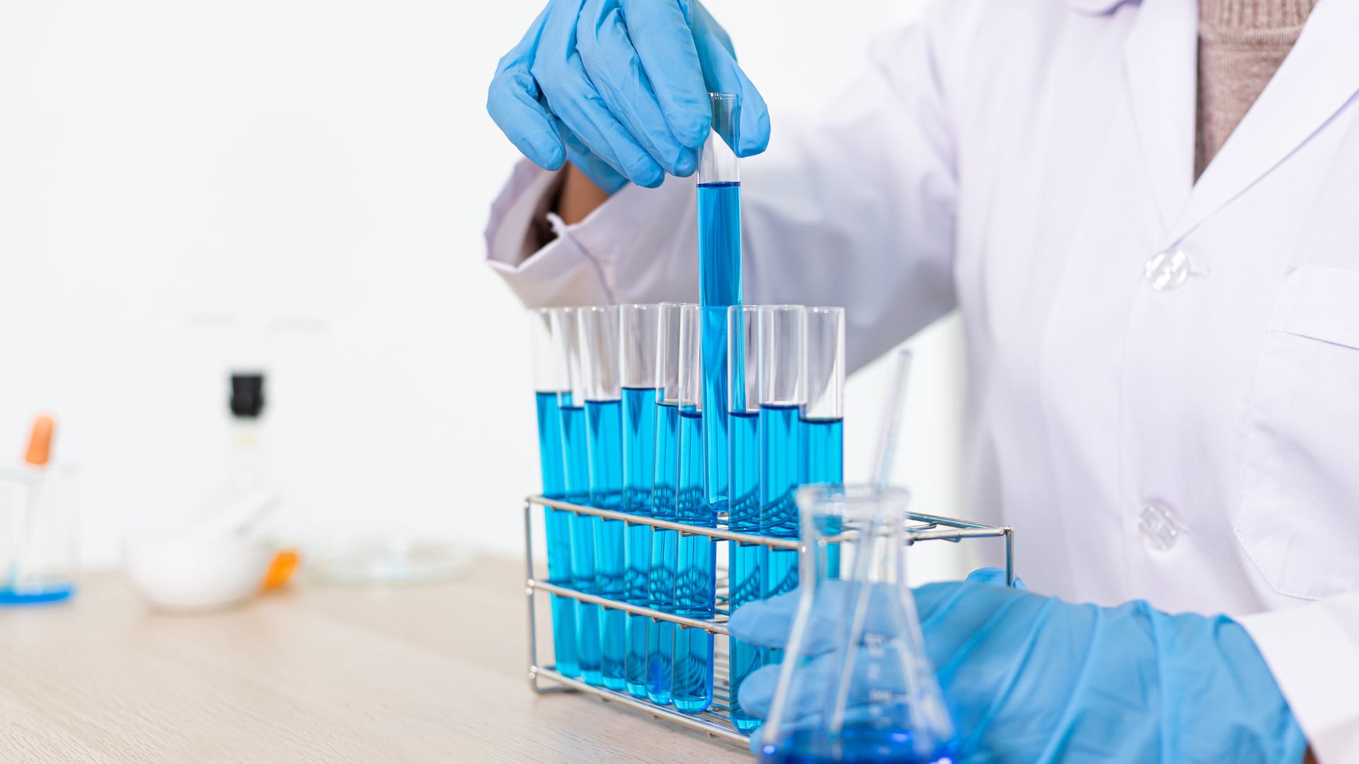 Imagen de una persona manipulando productos químicos de color azul con guantes de nitrilo azules en su lugar de trabajo 