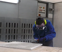 Imagen de un trabajador con equipo de protección en rostro, cortando una pieza de marmol